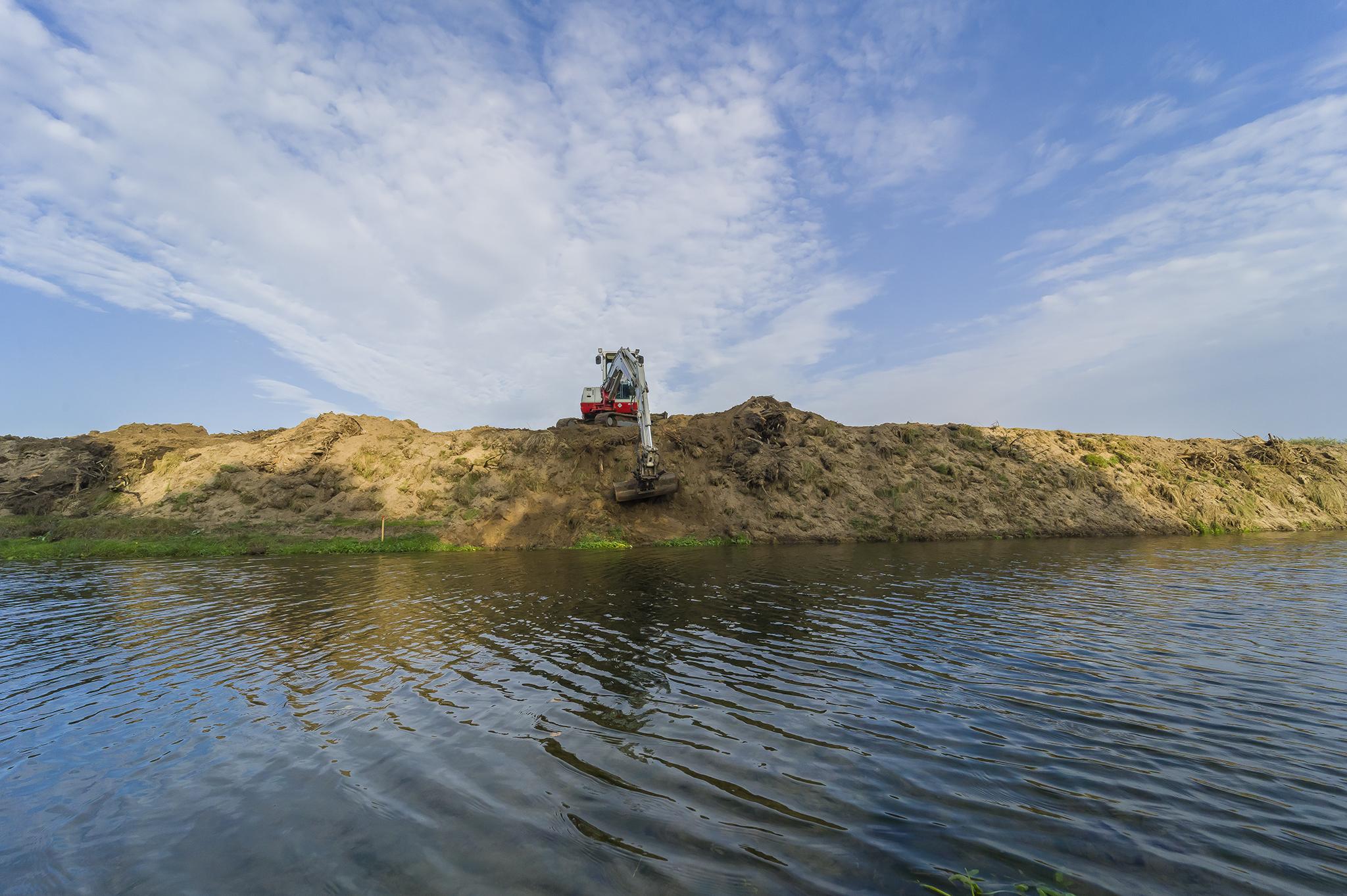 Graafmachine staat op oever aan het kanaal en graaft zand omhoog