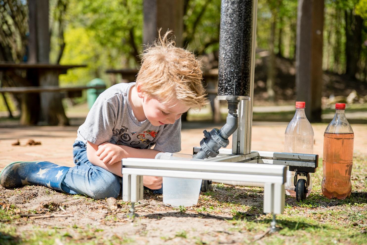 Een glimlachend kind kijkt aandachtig toe terwijl het leert hoe een waterfilter werkt.