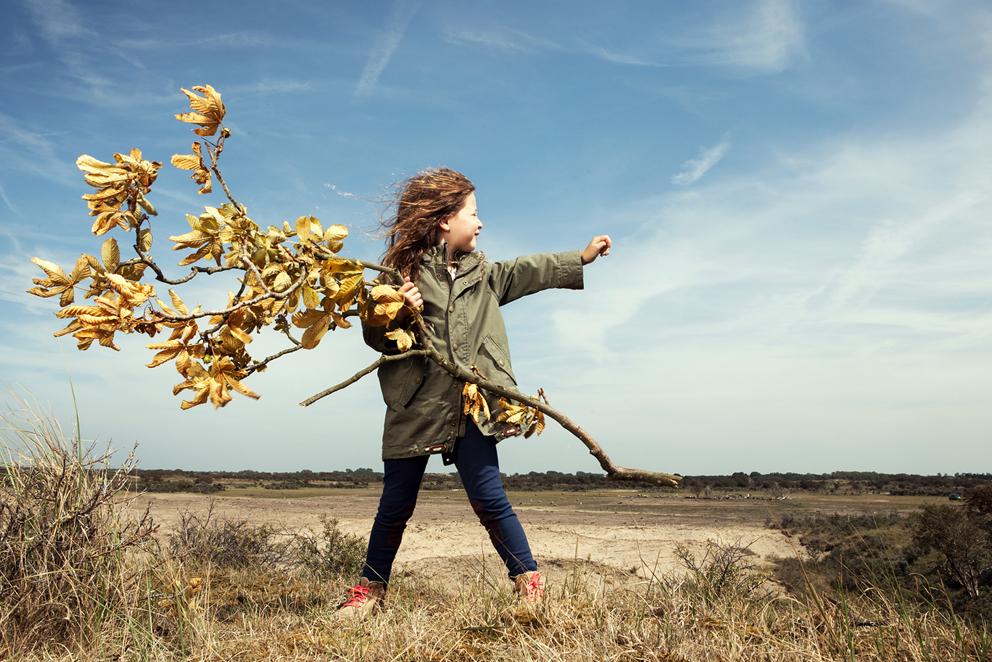 Kind met tak met dorre bladeren staat in de wind