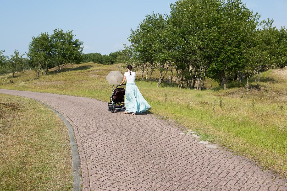 Vrouw wandelend met kinderwagen op een klinkerpad.