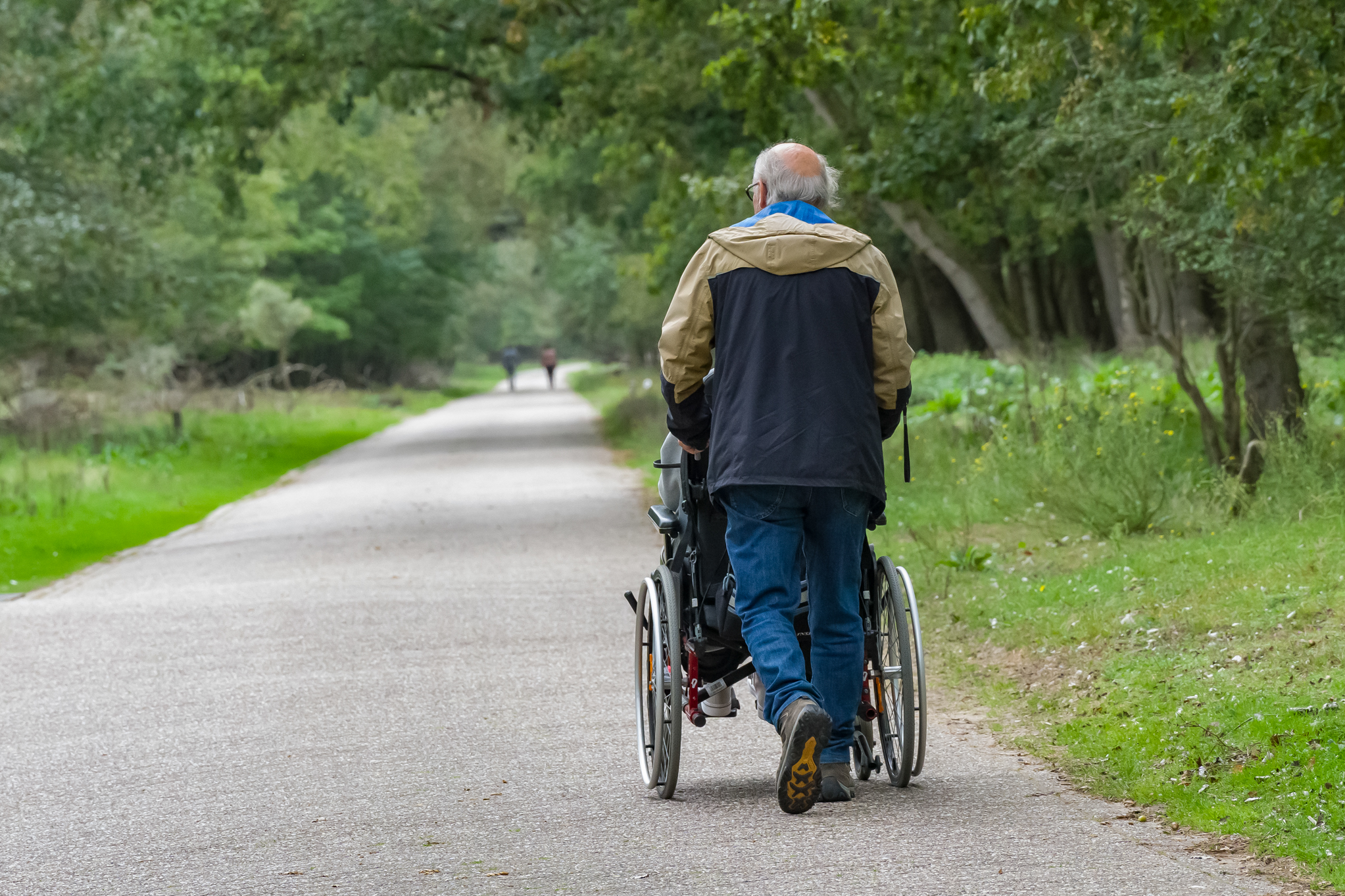 Man duwt een rolstoel voort op een klinkerweg in de duinen.