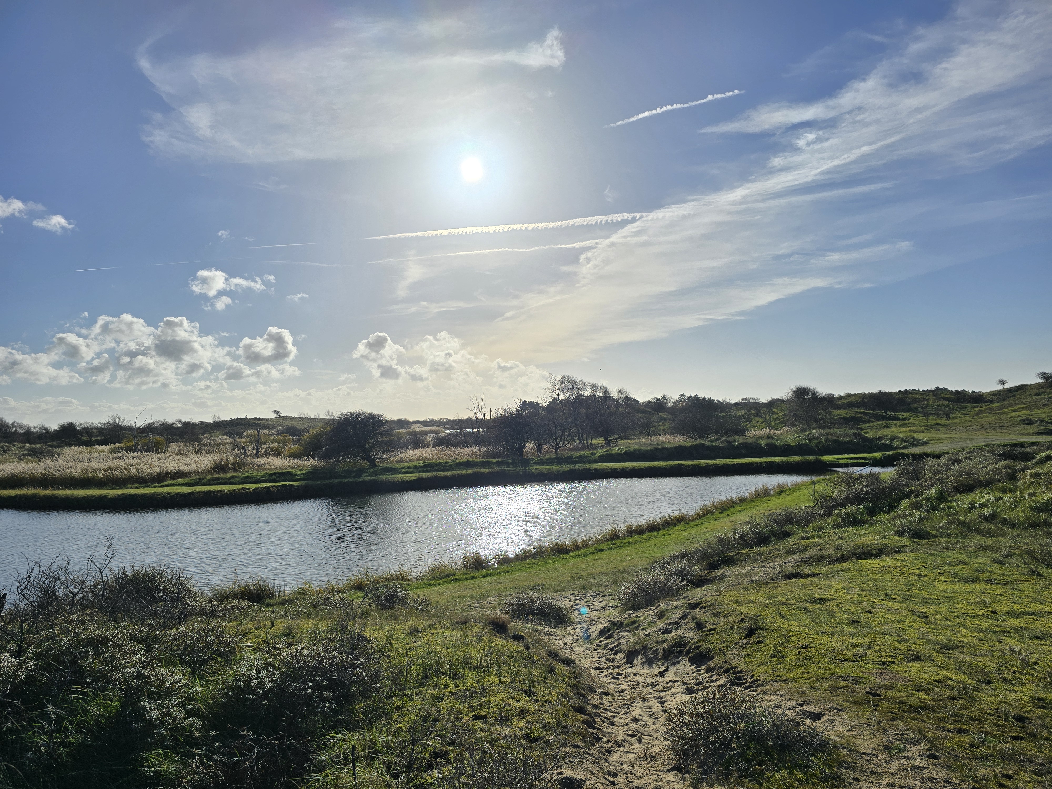 Uitzicht over een toevoersloot met blauwe lucht en stralend zonlicht